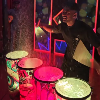 The pure joy of the liquid drum performance. A drummer is captured mid-laugh as he creates a splash of illuminated water with a powerful beat.