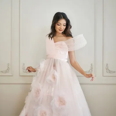 Introducing 'Carol', a dreamy pink ball gown. It features a sheer tulle skirt with 3D floral accents and a uniquely structured, wired drape on the bodice.