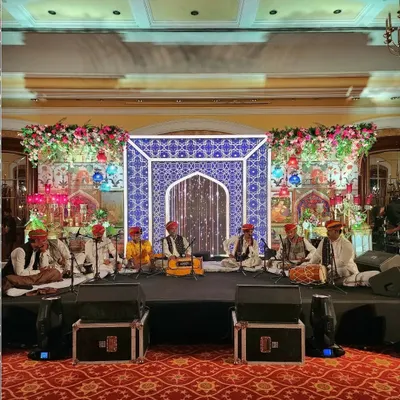 The stage for a Sufi Night, featuring a live Qawwali band. The backdrop is a custom-designed panel with intricate blue and white jaali patterns, flanked by vibrant floral arrangements to create an authentic and mesmerizing setting.