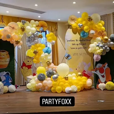 A charming Winnie the Pooh themed baby shower. The setup includes character cutouts, a custom backdrop with a quote, and a flowing yellow and white balloon arrangement.