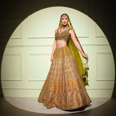 A truly regal bridal lehenga, captured in the spotlight. This opulent gold creation features extensive hand-embroidery, perfect for the bride who wants to feel like royalty.