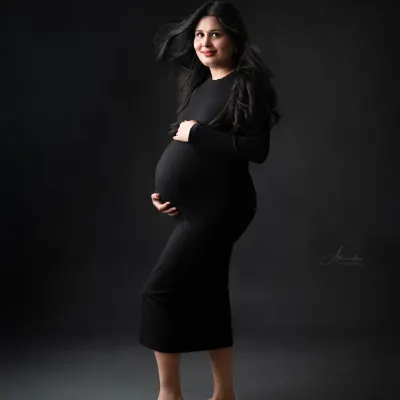 A powerful and modern solo portrait. The mom-to-be stands confidently in a simple black bodycon dress, with her hair blowing for a dynamic effect.