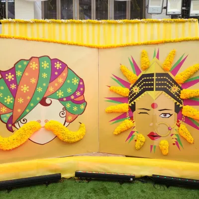 A funky and artistic photo booth for a Haldi ceremony. This backdrop features quirky illustrations of a bride and groom, with 3D elements made from fresh genda phool (marigolds).