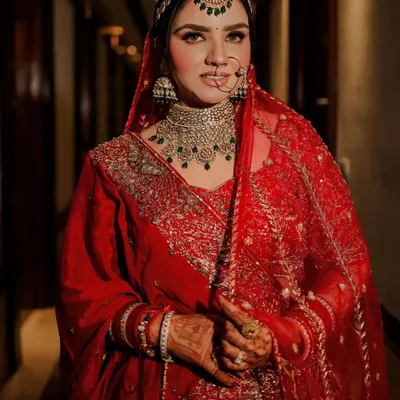 A classic bridal portrait that captures the bride's confident gaze and radiant glow. Her traditional red lehenga, intricate diamond and emerald jewelry, and elegant nath are all beautifully highlighted.