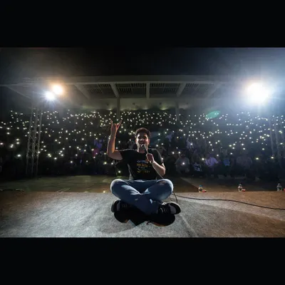 Comedian Samay Raina seated on stage, addressing a massive audience holding up their phone lights at Dhruva, IIM Trichy. This shot captures the incredible connection he builds with students.