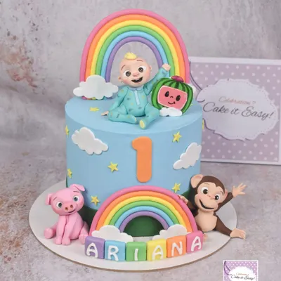 A vibrant Cocomelon cake for a first birthday, complete with JJ, the watermelon, a friendly monkey, and a pig. The double rainbow and colourful name blocks make it extra cheerful.