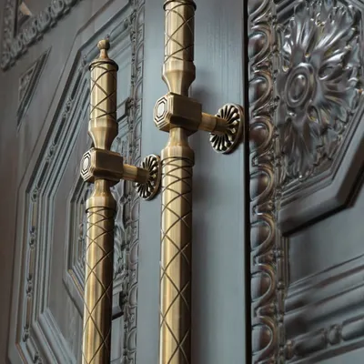 A closer look at the Raga Door Pull in an Antique Brass Finish. The neo-classical design features intricate cross-hatching and octagonal details that harmonize perfectly with the door's traditional carved panels, creating a cohesive and regal entryway.