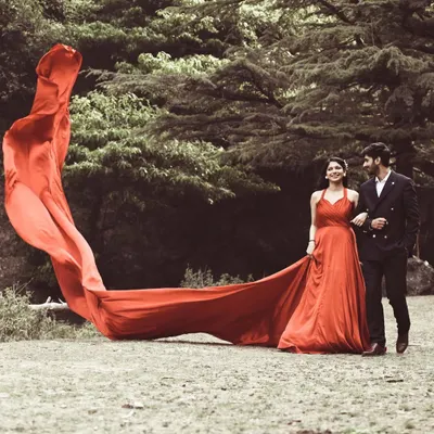 A dramatic pre-wedding portrait in a forest setting, with the bride's long red trail creating a stunning visual effect.