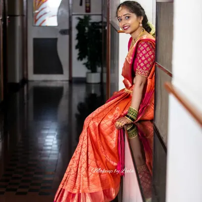 A beautiful bride ready for her Muhurtham ceremony. Her look features classic South Indian bridal makeup with a focus on radiant skin and defined eyes, paired with a stunning orange and pink silk saree.
