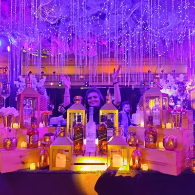 A wide shot of the spectacular Great Gatsby bar, fully lit for an evening of celebration. A happy team member celebrates behind the counter, which is adorned with lanterns, candles, and a stunning overhead light installation.