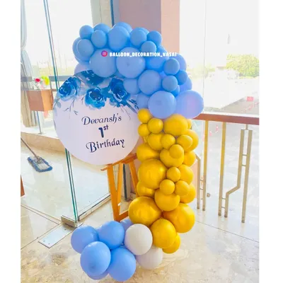 A beautiful welcome display for Devansh's first birthday. The personalized circular sign is framed by a cascade of blue, yellow, and white balloons, creating an elegant entrance for guests.