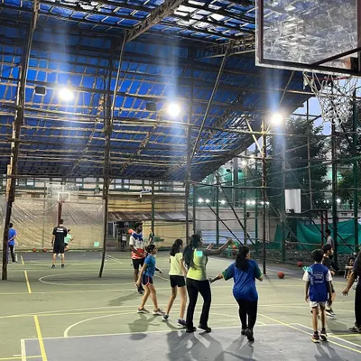 A view of a mixed-gender group enjoying an evening game. The powerful floodlights illuminate the entire court, and the blue covering ensures your game is never called off due to rain.