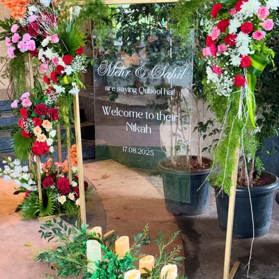A modern and elegant welcome sign for Mehr and Sahil's Nikah, printed on a clear acrylic board and framed with beautiful, vibrant floral arrangements.