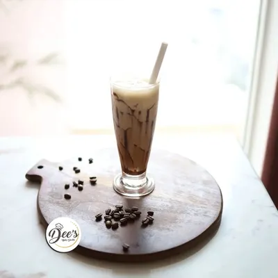 Savor the chill with every sip of our creamy cold coffee. It's the perfect refreshing escape, presented beautifully on a wooden board with coffee beans.