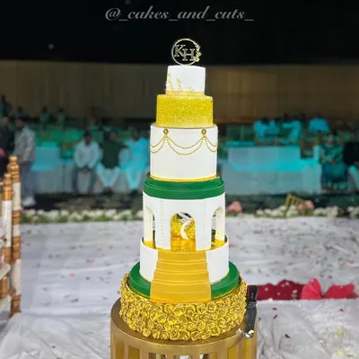 A full view of our royal engagement cake, standing tall at the celebration venue. The combination of white, gold, and green tiers with intricate details makes it a truly grand statement piece.