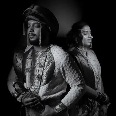 A powerful, royal-themed black and white portrait of a couple in traditional Peshwai attire, emphasizing their regal presence and the rich textures of their outfits.