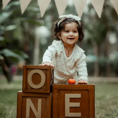 A joyful first birthday portrait of a baby girl with "ONE" blocks. Her happy expression and the rustic outdoor setting make this a perfect milestone photo.