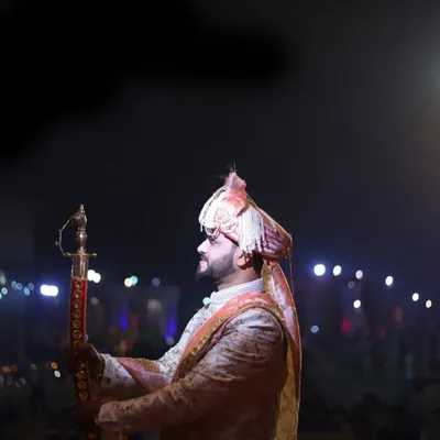 A dramatic and cinematic portrait of the groom during his wedding entrance at night, holding a traditional sword.
