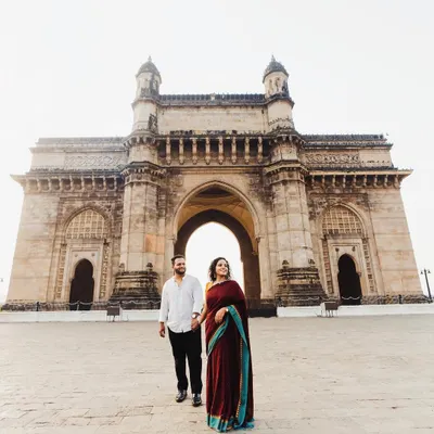 A grand, wide-angle shot featuring the couple at the Gateway of India. This image is a classic Mumbai pre-wedding photograph, celebrating their love story in the heart of the city.