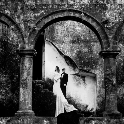 A black and white portrait that uses the strong arches of the ruins to frame the couple. The high contrast and shadows create a timeless, dramatic feel, focusing purely on their presence and the historic atmosphere.