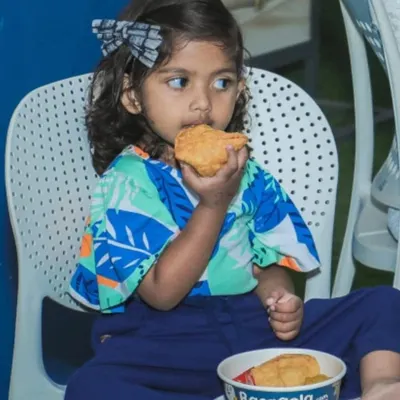 It brings me so much joy to see the little ones enjoying my food. Here, a young customer is happily munching on a crispy snack from my kitchen, a testament to flavors that everyone in the family can love.