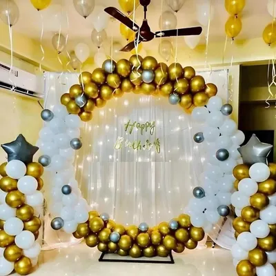 A stunning birthday celebration I designed, featuring a circular balloon arch in metallic gold, white, and silver. The sheer curtain backdrop with integrated fairy lights adds a warm, magical glow to the entire setup, making it a perfect photo corner for any home party.