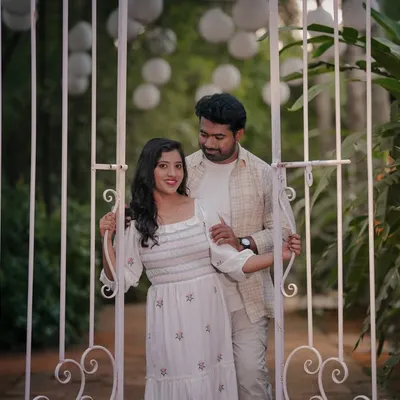 A romantic moment for a couple in matching white outfits, framed by a white garden gate.