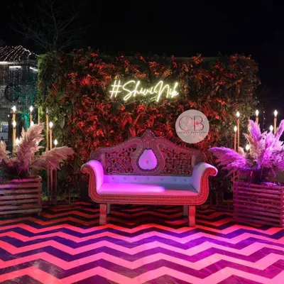 We set the stage for a memorable Sangeet night with this stunning photo booth. The design combines a lush green wall, pampas grass arrangements, and a custom neon hashtag, all set against a vibrant chevron-patterned dance floor.