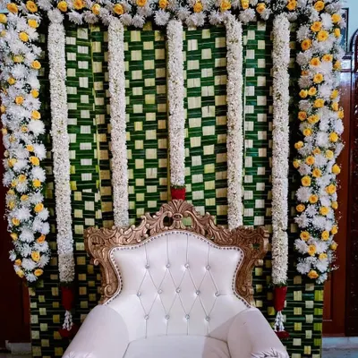 A complete traditional seemantha stage. The backdrop is made of woven coconut leaves, framed with white and yellow flowers, and features an elegant, tufted chair for the main ceremony.