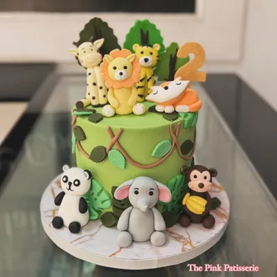 A vibrant jungle theme cake for a second birthday, surrounded by handcrafted fondant animals. A friendly lion, tiger, panda, elephant, monkey, and giraffe gather for a wild celebration.