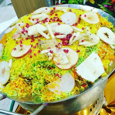 A large pan of colorful Kashmiri Pulao, a fragrant rice dish garnished with fresh fruits like apple and pomegranate. This is a visually appealing and delicious main course option.