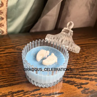 A beautiful baby boy announcement candle in a crystal jar. The wax is colored blue and topped with tiny baby feet embeds, making it a super cute and affordable favor.