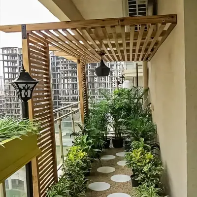 A charming balcony featuring a wooden pergola with hanging lanterns. The space is filled with potted plants, creating a private and lush garden feel in an urban setting.