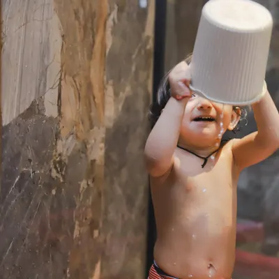 The pure joy of splashing! A toddler pours a bucket of water over his head, and we captured the exact moment of delight.