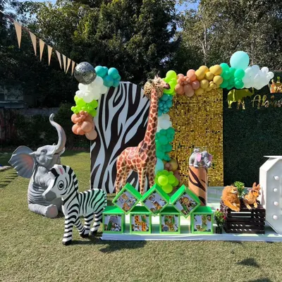 A fantastic outdoor jungle safari photo booth with a gold sequin wall, zebra-print panel, and life-sized giraffe, zebra, and elephant props.