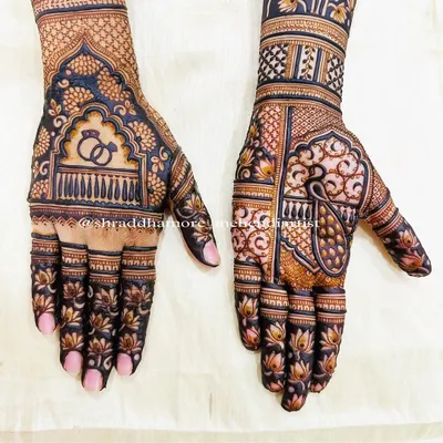 A classic bridal design featuring engagement rings under a royal arch on one hand and a majestic peacock on the other. The patterns are dense with lotus flowers and geometric checks.