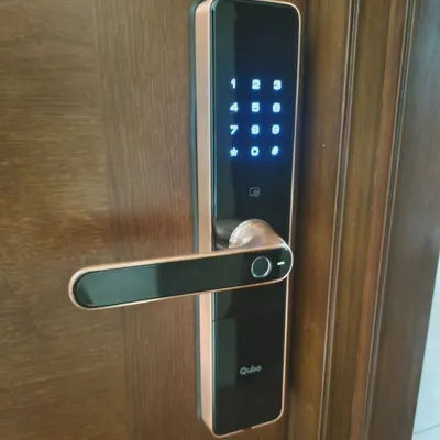 A close-up of a newly installed Qubo smart door lock. Notice the illuminated touch keypad and the integrated fingerprint sensor on the handle for quick, one-touch access.