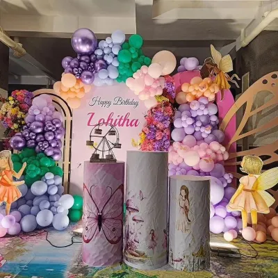 An elaborate fairy and butterfly themed birthday for Lohitha. This enchanting setup features a rainbow of pastel balloons, fairy wing props, and custom-printed plinths with magical illustrations.