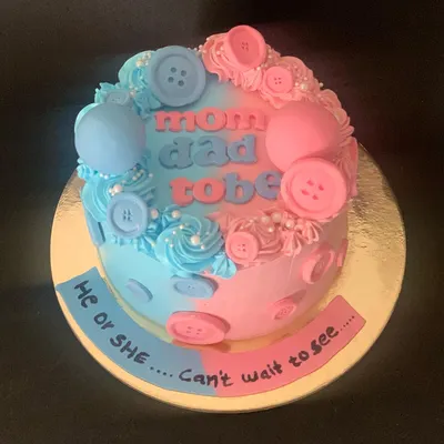 A "He or She" gender reveal cake. The cake is split into pink and blue, decorated with cute buttons, and asks the question "Can't wait to see!".