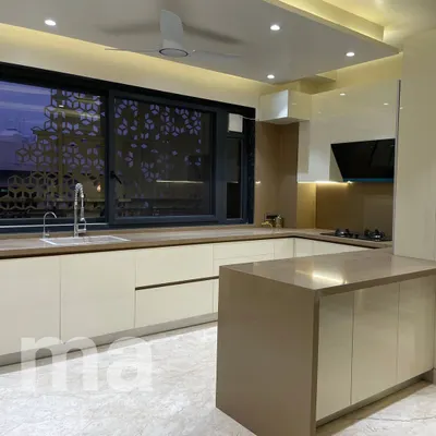 This open kitchen features an island that provides extra counter space and casual seating. The handleless cabinets are finished in a light, neutral color, creating a seamless and minimal look.