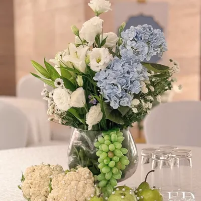 An artistic centerpiece for a 'Sehrabandi' ceremony, featuring cauliflower, pearl-studded green apples, and grapes alongside a bouquet of white and blue flowers. This is a perfect example of turning everyday produce into high art.