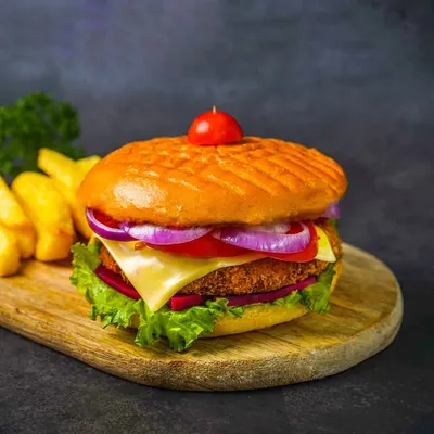 A picture-perfect burger with a veggie patty, cheese, lettuce, tomato, and onion, served with fries on a wooden board against a dark background.
