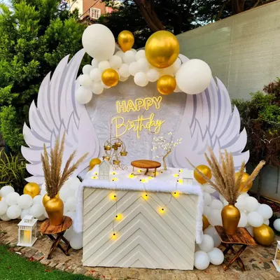An ethereal angel wings backdrop for a birthday celebration. This heavenly setup in white and gold includes a custom-designed table, pampas grass, and a "Happy Birthday" sign, creating a truly unique photo opportunity.