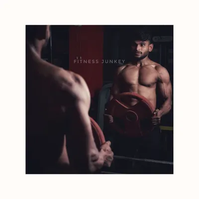 A classic shot for a bodybuilding portfolio, using a mirror to capture both the reflection and the subject. The dramatic lighting highlights the muscle definition in the back and arms while holding a weight plate.