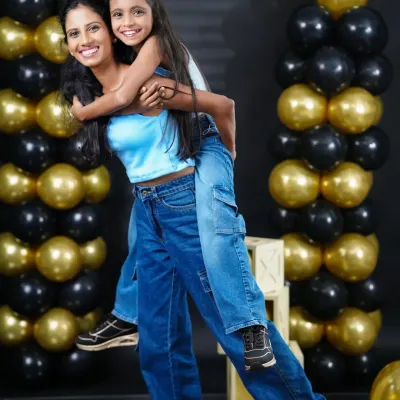 A fun piggyback ride between sisters during a birthday photoshoot. Our studio with black and gold balloon pillars provides a chic and celebratory setting.