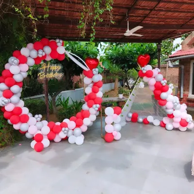 This heart-shaped balloon arch is a romantic choice for an outdoor anniversary party. The design, shown here in red, white, and silver, is set up on a covered patio, demonstrating its versatility for different outdoor spaces.