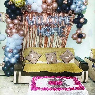A stylish 'Welcome Home' decoration in black, silver, and rose gold. The balloon arch over the sofa, combined with a shimmery curtain and flower petal art on the table, creates a chic and celebratory look.