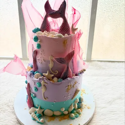 An enchanting two-tier mermaid cake. I used shades of pastel purple, pink, and teal, and decorated it with handcrafted mermaid tails, seahorses, and seashells.