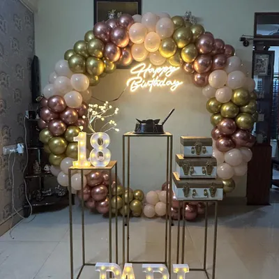 An elegant 18th birthday celebration with a rose gold, gold, and pastel pink balloon arch. The setup includes tall plinths, marquee numbers, and a neon sign.