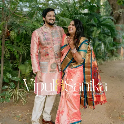 A joyful, full-length portrait of a couple in beautiful pink and gold traditional outfits, laughing together in a park. This image, with their names overlaid, is perfect for an engagement announcement.